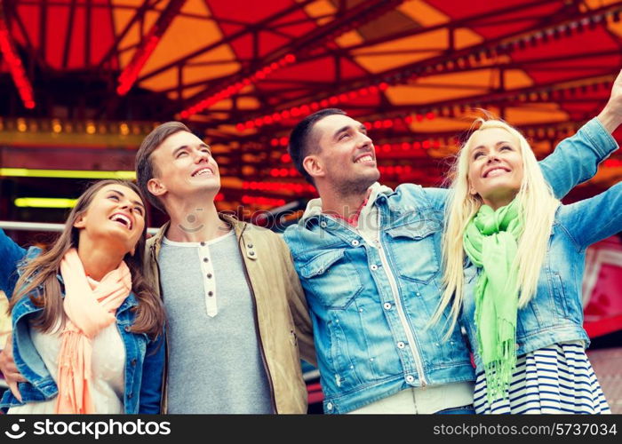 leisure, amusement park and friendship concept - group of smiling friends with carousel on the back