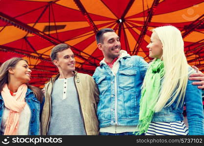 leisure, amusement park and friendship concept - group of smiling friends with carousel on the back