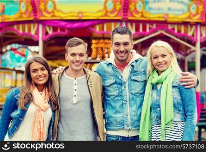 leisure, amusement park and friendship concept - group of smiling friends with carousel on the back