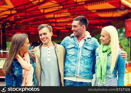 leisure, amusement park and friendship concept - group of smiling friends with carousel on the back