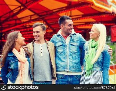 leisure, amusement park and friendship concept - group of smiling friends with carousel on the back