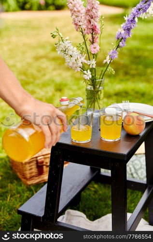 leisure and drinks concept - close up of female hand pouring fruit juice from bottle to glass on picnic at summer park. hand pouring juice to glass on picnic at park