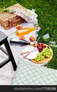 leisure and drinks concept - close up of food, drinks and basket on picnic blanket on grass. food, drinks and basket on picnic blanket on grass