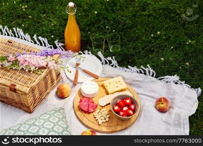 leisure and drinks concept - close up of food, drinks and basket on picnic blanket on grass. food, drinks and basket on picnic blanket on grass