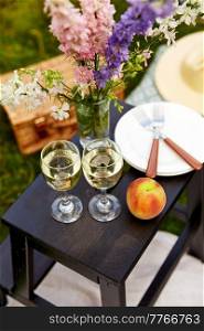 leisure and drinks concept - close up of picnic basket, flowers and glasses of champagne on wooden stool at park. picnic basket, flowers and wine glasses at park