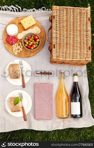 leisure and eating concept - close up of food, drinks and picnic basket on blanket on grass at summer park. food, drinks and picnic basket on blanket on grass