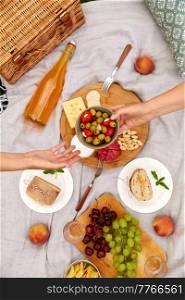leisure and eating concept - close up of hands holding bowl with olives above food and drinks on picnic blanket. close up of hands with food and drinks on picnic