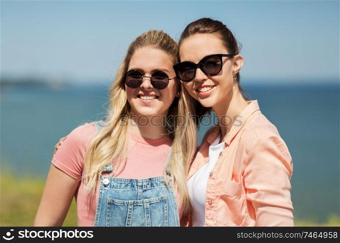leisure and friendship concept - happy smiling teenage girls or best friends in sunglasses at seaside in summer. teenage girls or best friends at seaside in summer