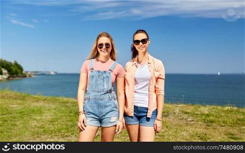 leisure and friendship concept - happy smiling teenage girls or best friends in sunglasses at seaside in summer. teenage girls or best friends at seaside in summer