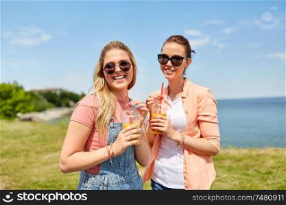 leisure and friendship concept - happy smiling teenage girls or best friends in sunglasses with smoothie drinks at seaside in summer. teenage girls or friends with drinks in summer