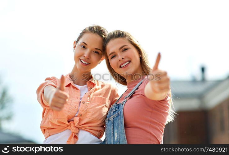 leisure and friendship concept - happy smiling teenage girls or best friends showing thumbs up outdoors in summer. teenage girls or best friend showing thumbs up