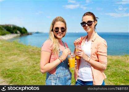 leisure and friendship concept - happy smiling teenage girls or best friends in sunglasses with smoothie drinks at seaside in summer. teenage girls or friends with drinks in summer