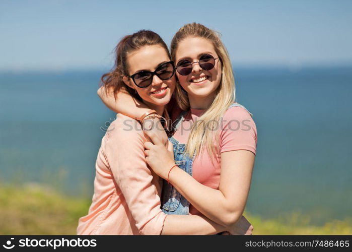 leisure and friendship concept - happy smiling teenage girls or best friends in sunglasses hugging at seaside in summer. teenage girls or best friends at seaside in summer