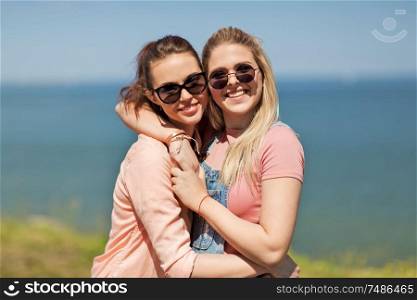 leisure and friendship concept - happy smiling teenage girls or best friends in sunglasses hugging at seaside in summer. teenage girls or best friends at seaside in summer
