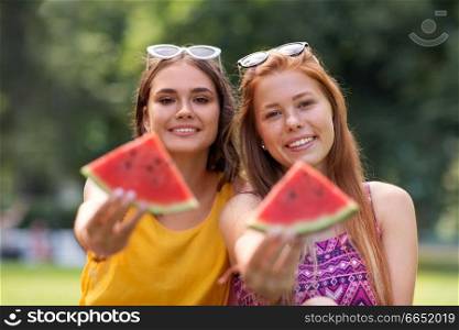 leisure and friendship concept - happy smiling teenage girls or friends eating watermelon at picnic in summer park. teenage girls eating watermelon at picnic in park