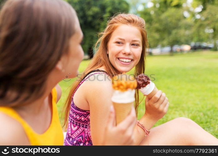 leisure and friendship concept - happy smiling teenage girls or friends eating ice cream at picnic in summer park. teenage girls eating ice cream at picnic in park