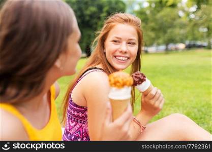 leisure and friendship concept - happy smiling teenage girls or friends eating ice cream at picnic in summer park. teenage girls eating ice cream at picnic in park