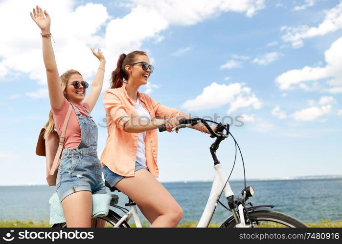 leisure and friendship concept - happy smiling teenage girls or friends riding bicycle together at seaside in summer. teenage girls or friends riding bicycle in summer