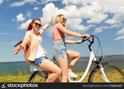 leisure and friendship concept - happy smiling teenage girls or friends riding bicycle together at seaside in summer. teenage girls or friends riding bicycle in summer