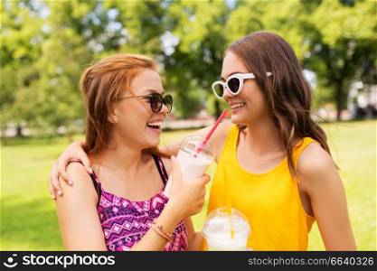leisure and friendship concept - happy smiling teenage girls or friends with milk shakes or smoothie drinks at summer summer park. teenage girls with milk shakes at summer park