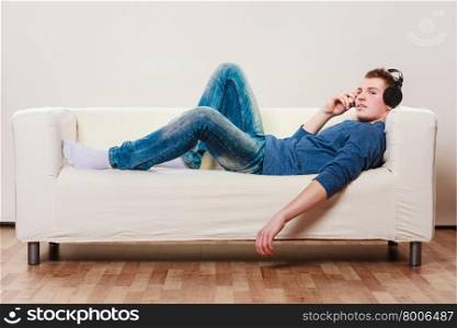 leisure and lifestyle concept. Young handsome man with headphones lying on couch listening music at home