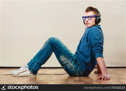 leisure and lifestyle concept. Young hipster man fashion clothes with headphones sitting on floor listening music.