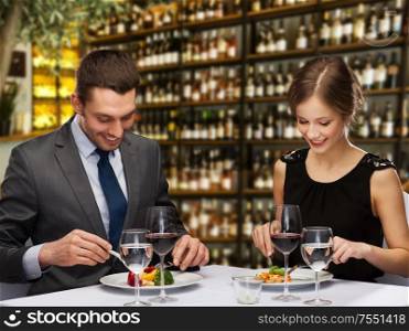 leisure and luxury concept - smiling couple eating main course over restaurant or wine bar background. smiling couple eating main course at restaurant
