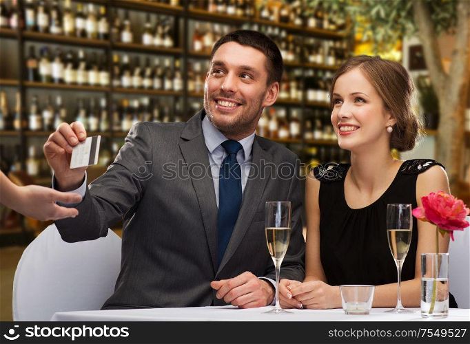 leisure and luxury concept - smiling couple paying for dinner with credit card over restaurant or wine bar background. hsppy couple paying with credit card at restaurant