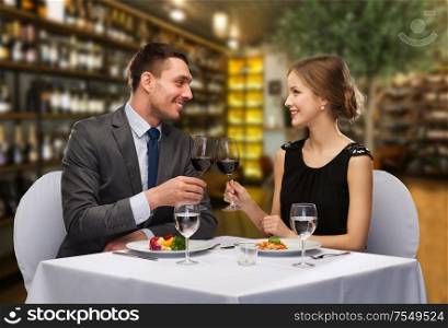 leisure and luxury concept - smiling couple with food clinking glasses of red wine over restaurant background. smiling couple clinking wine glasses at restaurant