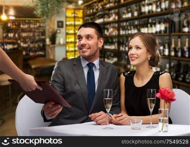 leisure and luxury concept - waiter giving menu to happy couple over restaurant or wine bar background. waiter giving menu to happy couple at restaurant