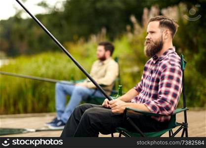 leisure and people concept - bearded man with friend fishing at lake. bearded man with friend fishing at lake
