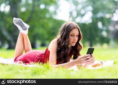 leisure and people concept - beautiful young woman with smartphone lying on picnic blanket at summer park. beautiful young woman with smartphone at park