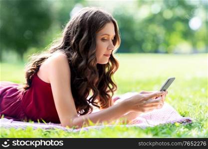 leisure and people concept - beautiful young woman with smartphone lying on picnic blanket at summer park. beautiful young woman with smartphone at park