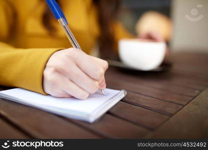 leisure and people concept - close up of young woman drinking cocoa and writing to notebook at city street cafe. close up of hand writing to notebook at cafe