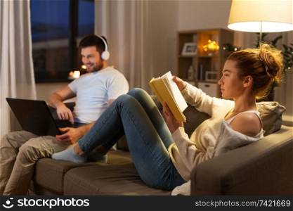 leisure and people concept - couple with laptop computer and book at home in evening. couple with laptop computer and book at home