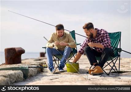 leisure and people concept - friends or fishermen adjusting fishing rods with bait on pier. friends adjusting fishing rods with bait on pier