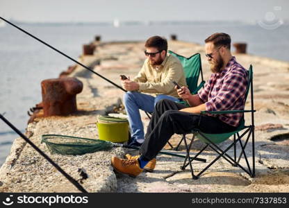 leisure and people concept - friends with smartphones fishing on pier at sea. friends with smartphones fishing on pier at sea