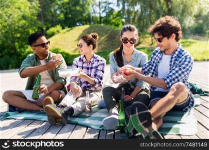 leisure and people concept - group of happy friends with drinks and food having picnic at summer park. happy friends having picnic at summer park