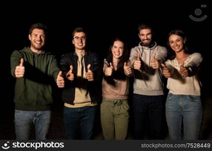 leisure and people concept - group of happy smiling friends showing thumbs up outdoors at night. happy smiling friends showing thumbs up at night