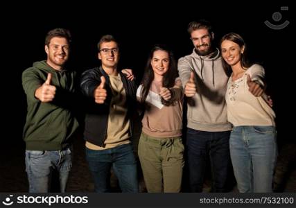 leisure and people concept - group of happy smiling friends showing thumbs up outdoors at night. happy smiling friends showing thumbs up at night