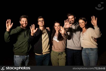 leisure and people concept - group of happy smiling friends waving hands outdoors at night. happy smiling friends waving hands at night