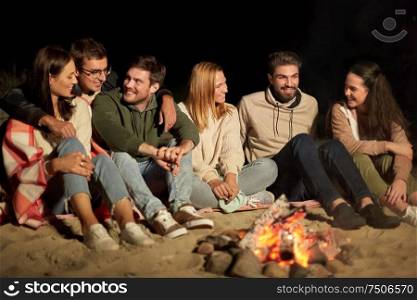 leisure and people concept - group of smiling friends sitting at camp fire on beach at night. group of friends sitting at camp fire on beach