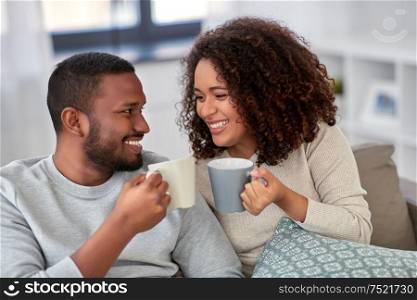 leisure and people concept - happy african american couple drinking coffee or tea at home. african american couple drinking coffee at home