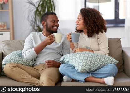 leisure and people concept - happy african american couple drinking coffee or tea at home. african american couple drinking coffee at home