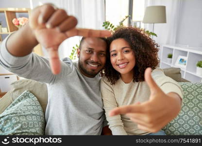 leisure and people concept - happy african american couple making selfie frame gesture at home. happy couple making selfie frame gesture at home