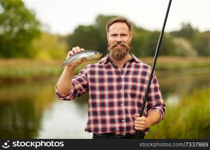 leisure and people concept - happy bearded fisherman with fishing rod and fish catch at lake or river. bearded fisherman with fishing rod and fish catch