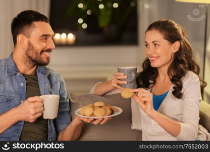 leisure and people concept - happy couple drinking tea or coffee with cookies at home. happy couple drinking tea with cookies at home