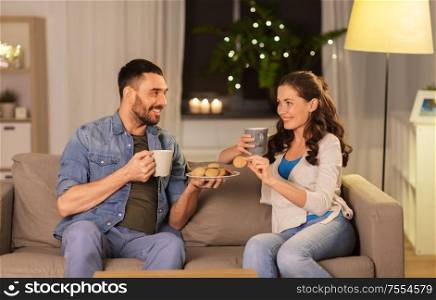 leisure and people concept - happy couple drinking tea or coffee with cookies at home. happy couple drinking tea with cookies at home