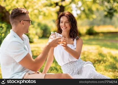 leisure and people concept - happy couple with drinks having picnic at summer park. happy couple toasting drinks at summer park