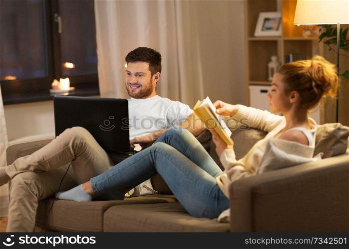 leisure and people concept - happy couple with laptop computer and book at home in evening. couple with laptop computer and book at home